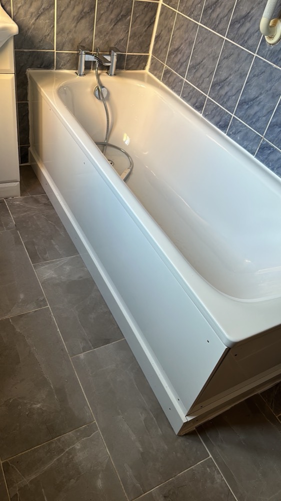 A newly fitted white bath with chrome mixer tap against slate-grey tiling and a tidy tiled floor, installed by Capital Flow Heating and Plumbing.