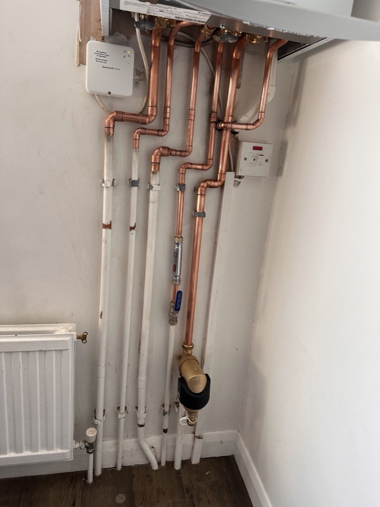 Neat copper central-heating pipework installed below a Vaillant boiler by Capital Flow Heating and Plumbing, with a Honeywell control and radiator alongside.