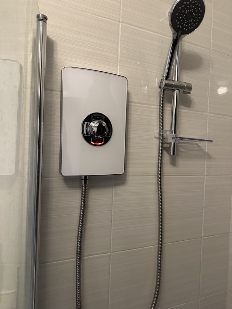 A white and chrome Triton electric shower fitted on cream tiles with a riser rail and handset, installed by Capital Flow Heating and Plumbing.